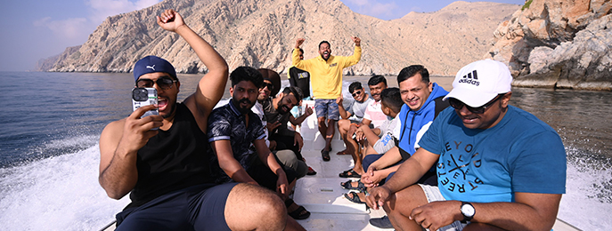 A traditional wooden boat carrying passengers on calm blue waters under a clear sky in Musandam 