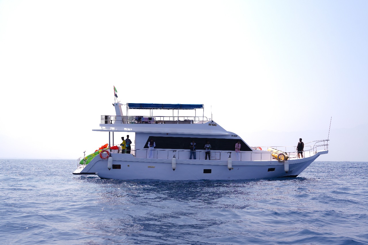 A traditional wooden boat carrying passengers on calm blue waters under a clear sky in Musandam 