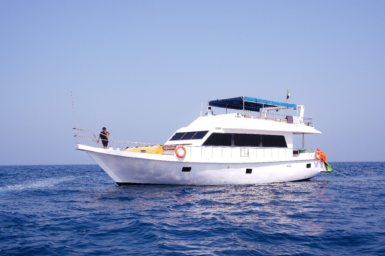 A traditional wooden boat carrying passengers on calm blue waters under a clear sky in Musandam 