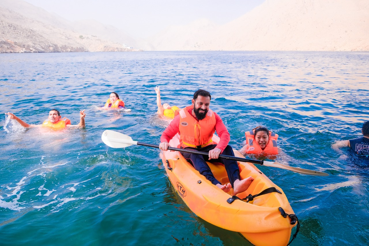 A traditional wooden boat carrying passengers on calm blue waters under a clear sky in Musandam 