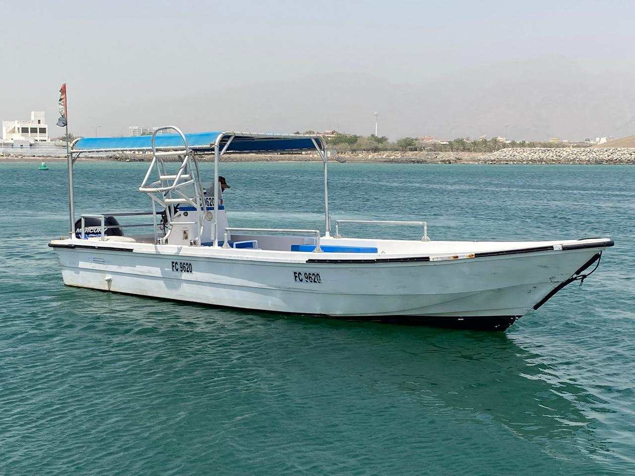 A traditional wooden boat carrying passengers on calm blue waters under a clear sky in Musandam 
